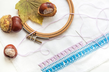 Mature chestnuts, autumn leaves and needlework on white background