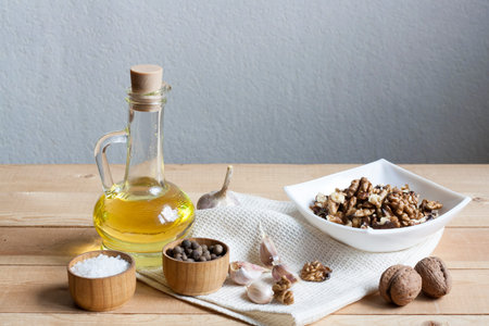 Walnuts in a white bowl, garlic, pepper salt and oil on a wooden background, wooden board and white napkinの写真素材