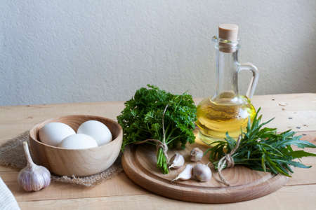 Food ingredients. Oil, eggs, garlic, limon, walnuts and herbs on wooden table. Wooden board and napkin.の写真素材