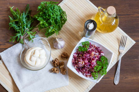Beetroot salad with walnuts and cream sauce. Nuts, garlic, salt, pepper, herbs, boiled eggs and oil on a wooden table.の写真素材