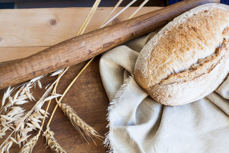 Freshly baked homemade bread on a wooden table. Next to the bread wheat and oats ears. Rustic style....