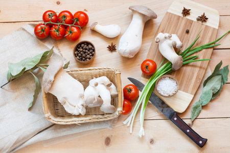Basket with eryngii mushrooms and ingredients for cooking on the wooden table of the kitchen backgroundの写真素材