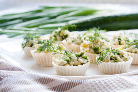 Tartlets with cheese and green onion filling decorated with dill on a dishの写真素材