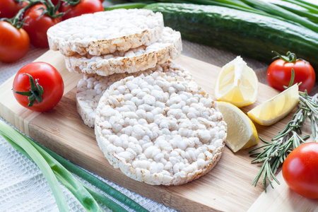 Plain rice cakes, galette rice with lemon, rosemary and vegetables on wooden board