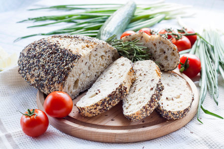 Sliced homemade bread loaf with sesame and other grains on a round desk at wooden table