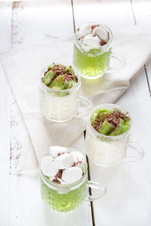 Jelly with kiwi fruit with marshmallows and grated chocolate in glass, sliced kiwi on white wooden tableの写真素材