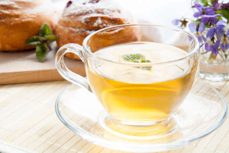 Cup of green tea with lemon balm and tasty rolls, blue spring flowers on light wooden backgroundの写真素材