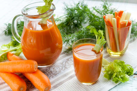Fresh carrot juice with carrots, celery, dill and parsley on light backgroundの写真素材