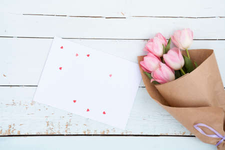 Beautiful bouquet of pink tulips next to a white envelope and pink sugar hearts on light wooden backgroundの写真素材