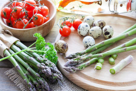 Bunch of fresh green asparagus spears on round board with tomatoes, quail eggs and parsleyの写真素材