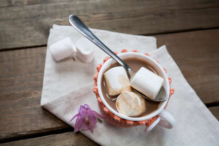 Hot cocoa with marshmallows in cup and cup crochet holder and fresh spring pink bell flowers on wooden tableの写真素材