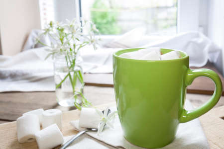 .Hot cocoa with marshmallows in green cup on napkin and fresh spring white flowers on wooden tableの写真素材