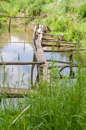 Old wooden bridge over the lake overgrown with grass. Old rural landscape.の写真素材
