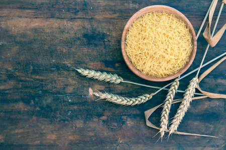 Uncooked Italian pasta Capellini in wooden pot with wheat ears on dark wooden background. Toned and processing photos with soft selective focus.の写真素材