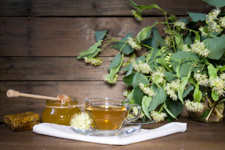 Linden tea in glass cup and jar with honey with linden flowers on a dark wooden backgroundの写真素材