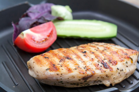 Grilled chicken breast steak with tomato, cucumber and violet basil on teflon pan grill, black slate...