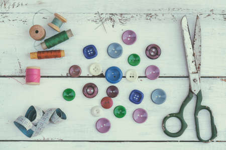 Set of several pied buttons for garment with threads, garment tape and scissors on a bright wooden background. Toned and processing photos with soft focus in vintage style.の写真素材