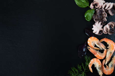 Preparing fresh seafood in the kitchen with gourmet pink shrimp and octopuses surrounded by fresh herbs and spices on black stone backgroundの写真素材