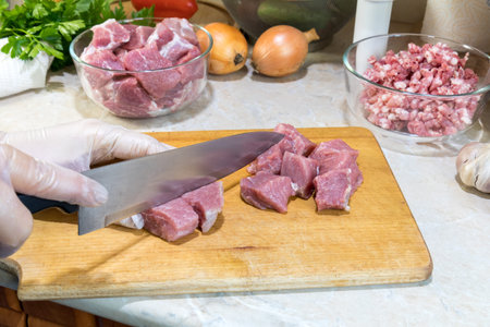 A woman is cutting fresh pork on a wooden cutting board in the modern kitchen surrounded by fresh...