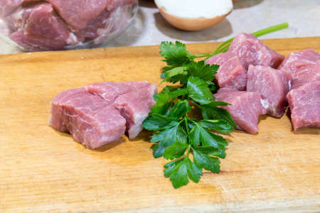 Raw pork neck meat cut in slices and fresh parsley on wooden cutting boardの写真素材
