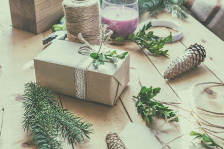 Wrapping eco Christmas packages with brown paper, string and natural branches and decor elements on wooden tableの写真素材