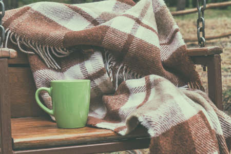 Wooden swing with wool blanket and green cup in autumn park. Coloring and processing photos in vintage style.の写真素材