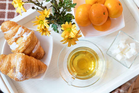 Cup of tea, croissant, chrysanthemum flowers and tangerines in tray on the table. Cozy home concept. Coloring and processing photoの写真素材