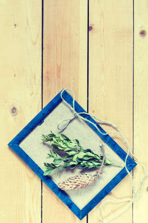 Craft supplies. Blue photo frame, boxwood, cone and rope on light wooden pine background. Coloring and processing photoの写真素材