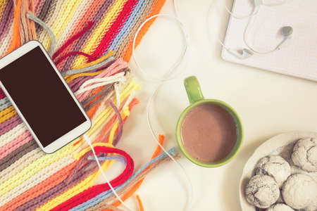 Office desk with cup of hot chocolate, phone, notebook, checkered scarf and chocolate cookies. Flat lay white background. Coloring and processing photo.の写真素材