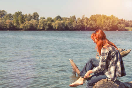 Young woman with red hair in checkered shirt and sunglasses at the river in the sunny day. Coloring and processing photo with soft focusの写真素材
