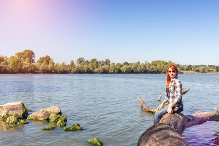 Young woman with red hair in checkered shirt and sunglasses at the river in the sunny day. Coloring and processing photo with soft focusの写真素材