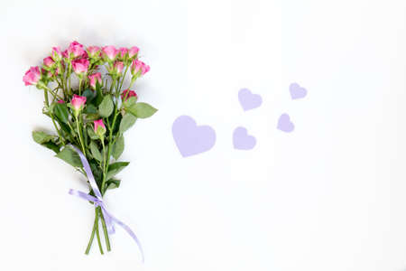 Fresh pink little roses and paper violet hearts. Flat lay on white background, top view.の写真素材