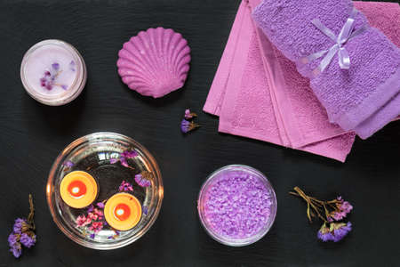 Spa products. Lavender bath salts, dry flowers, soap, cosmetic cream, candles and towel. Violet purple concept. Flat lay on black background, top view.の写真素材
