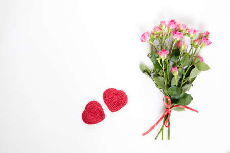 Fresh pink little roses with red ribbon and two red crochet heart. Flat lay on white background, top view.の写真素材