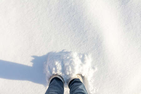 Woman foots in jeans and white boots in a large depth of snow. Sunshine on the snow real nature background.の写真素材