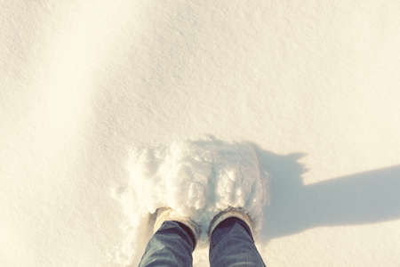 Woman foots in jeans and white boots in a large depth of snow. Sunshine on the snow real nature background.の写真素材