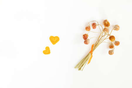 Dry little flowers with orange ribbon and two orange crochet heart. Flat lay on white background top view.の写真素材