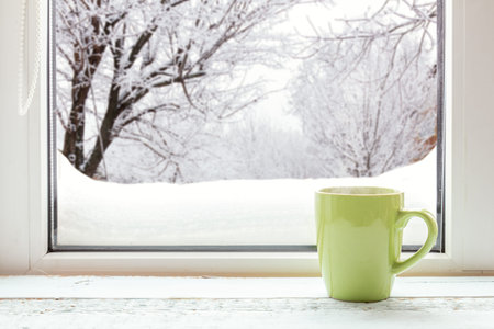 Cup of coffee on the window sill. In the background, a beautiful winter landscape in snow. Cozy home concept.の写真素材