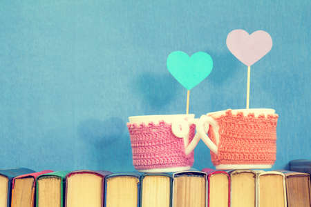 Valentines day concept. Two cups with blue paper heart and violet paper heart  on books over blue background.の写真素材
