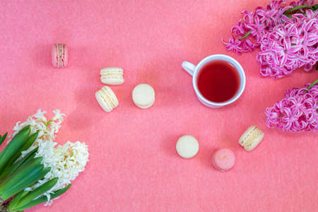Beautiful spring holiday background. Cup of tea, fresh white and pink hyacinth and sweet  berry and vanilla macaroons cookies on pink copy space groundwork.の写真素材