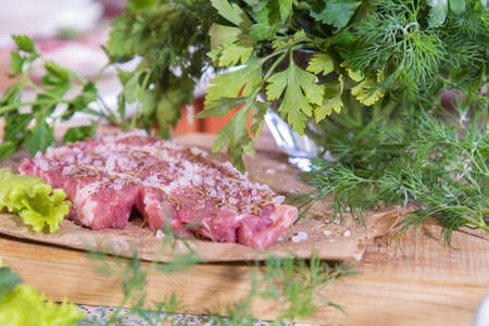 Fresh raw pork steak with salt and spices on paper. Fresh green dill and parsley.  Shallow depth of field. Coloring and processing photo.の写真素材