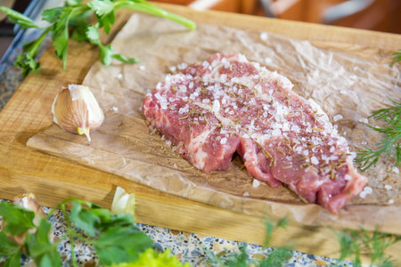 Fresh raw pork steak with salt and spices on paper. Fresh green dill and parsley.  Shallow depth of...