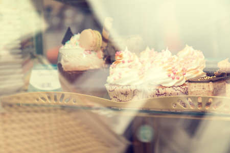 Cupcakes with vanilla cream on showcase in cafe under glass. Shallow depth of field. Toned.の写真素材