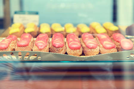 Many eclairs cakes on showcase in cafe. Eclairs with red and yellow glaze. Shallow depth of field. Toned.の写真素材