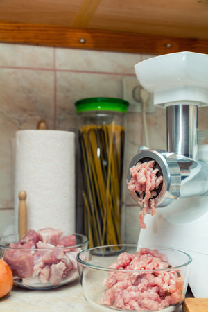 Home electric meat-grinder is making pork stuffing in a modern kitchen. Pork stuffing in a glass...