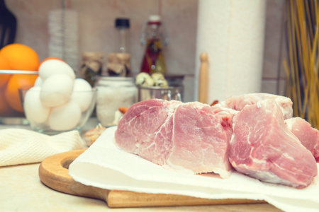 Raw pork neck meat cut in slices on wooden cutting board.  Shallow depth of field. Toned.