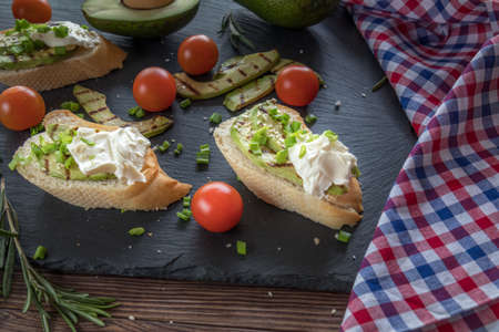 Bread with slices of grilled avocado and cream cheese on a black cutting stone board. Fresh parsley and rosemary. Vegetarian, vegan concept.の写真素材