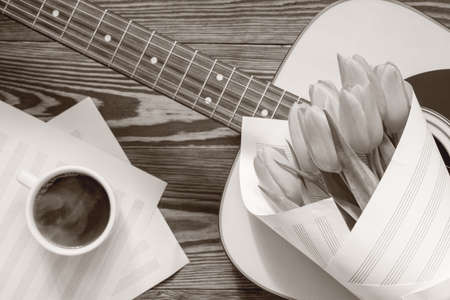 Beautiful spring background music. Guitar, yellow tulips, cup of coffee, musical page on a dark wooden background. Coloring and processing photo with old monochrome style.の写真素材
