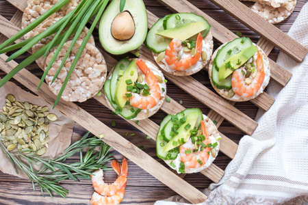 Rice cakes with sliced avocado cucumber shrimp and cream cheese.  Fresh parsley and rosemary. Vegetarian, vegan concept. Shallow depth of field. Coloring and processing photo.の写真素材