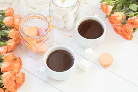 Orange mango macaroons, cup of coffee, marshmallow and fresh little roses on light wooden background. Sunlight. Coloring and processing photo with light vintage style. Shallow depth of field.の写真素材